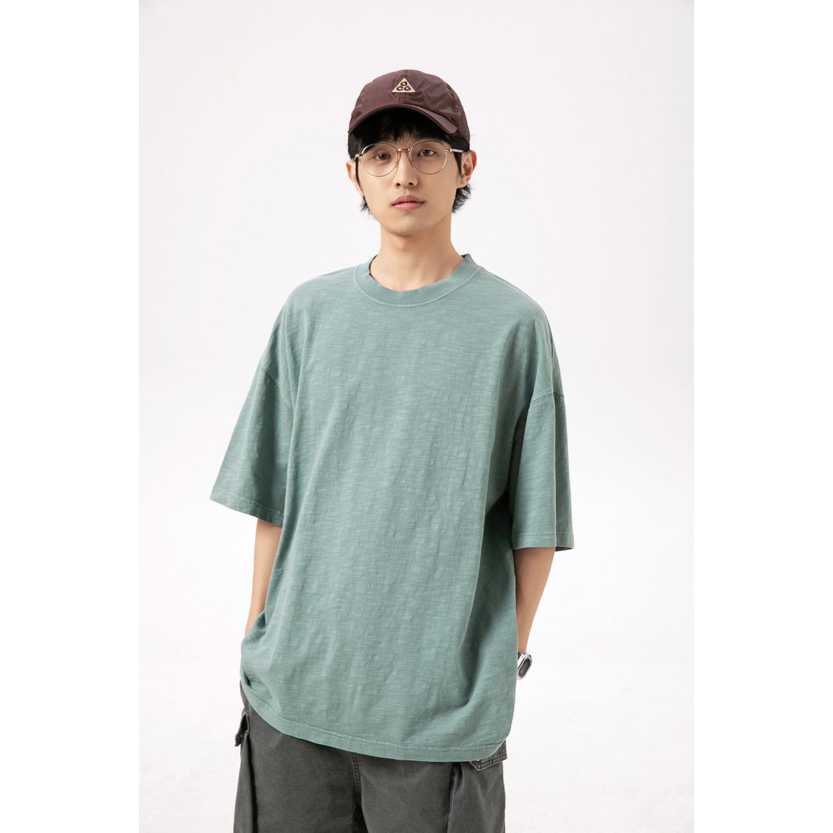 Front view of a man wearing an oversized muted teal T-shirt with a crew neck and short sleeves.