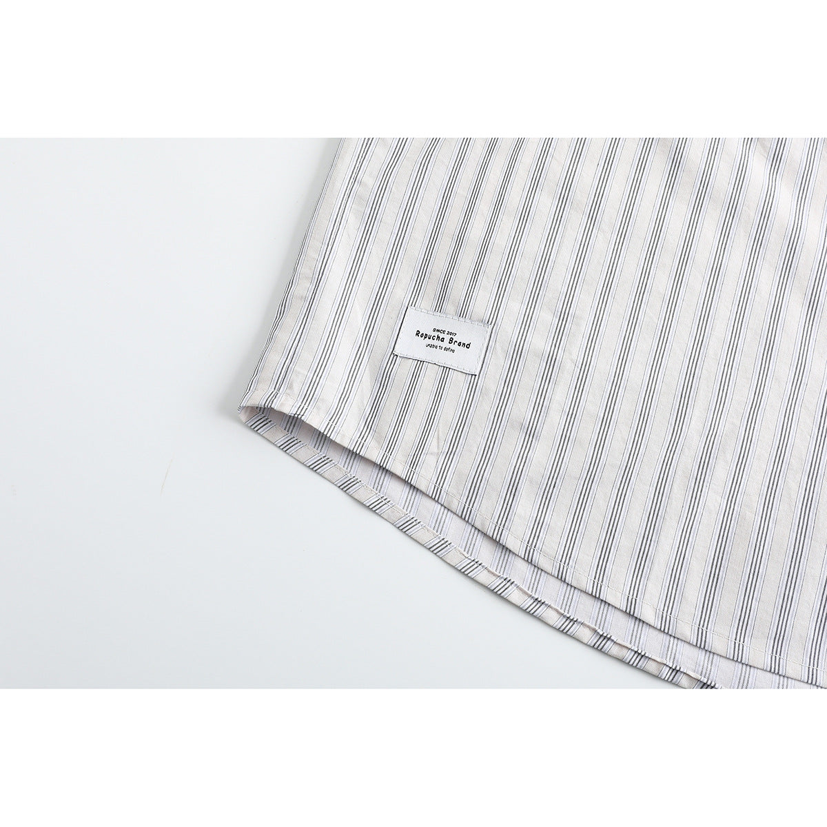 Close-up of the striped white shirt hem with a small sewn-on rectangular label.