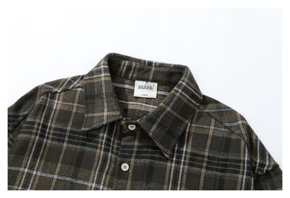 Upper front of a dark plaid button-up shirt with a pointed collar, cream buttons, and a neck label.