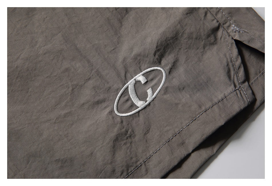Close-up of a white embroidered oval emblem near the hem of the charcoal-gray shorts.
