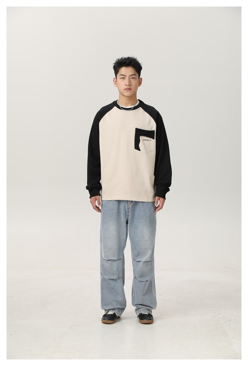Model wearing a beige sweatshirt with black raglan sleeves and chest pocket, with light-wash wide-leg jeans, front view