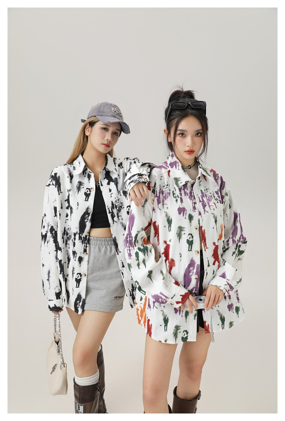 Two models wearing oversized printed shirts, one in black and white and one in purple, green and red on white