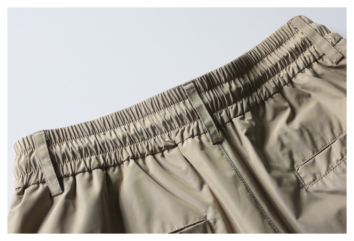 Close-up of taupe trousers with an elastic waistband, belt loops, fly seam, and pocket edges.