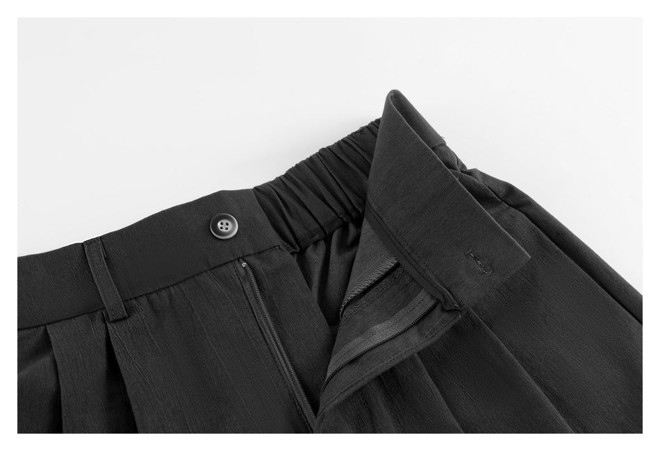 Close-up of black trousers showing the button, zipper fly, belt loop, and gathered elastic waistband.