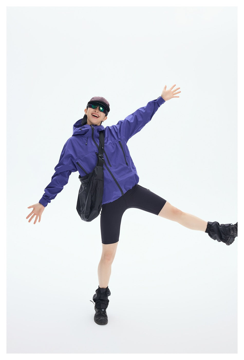 Model in a purple hooded jacket and black cycling shorts, posing with arms outstretched.
