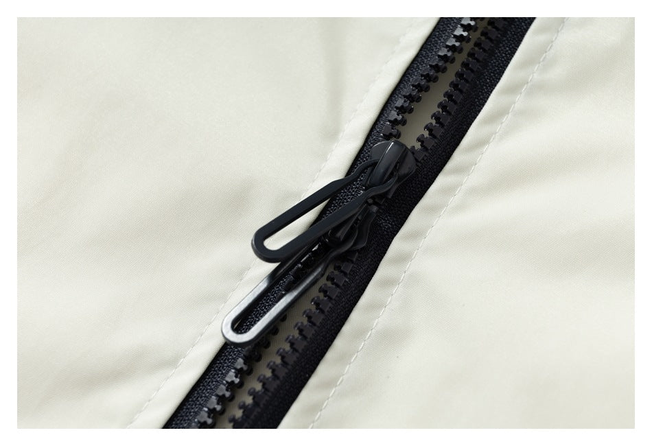 Close-up of a black two-way zipper on cream-colored garment fabric.