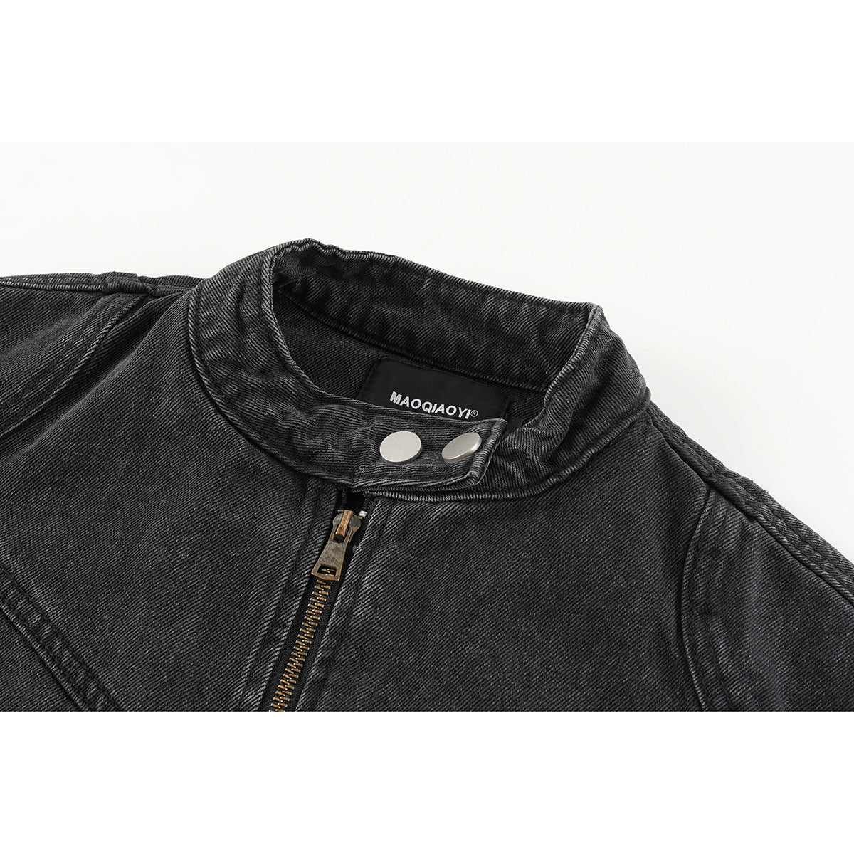 Close-up of a charcoal denim jacket collar with silver snaps, a brass zipper and a sewn-in neck label.