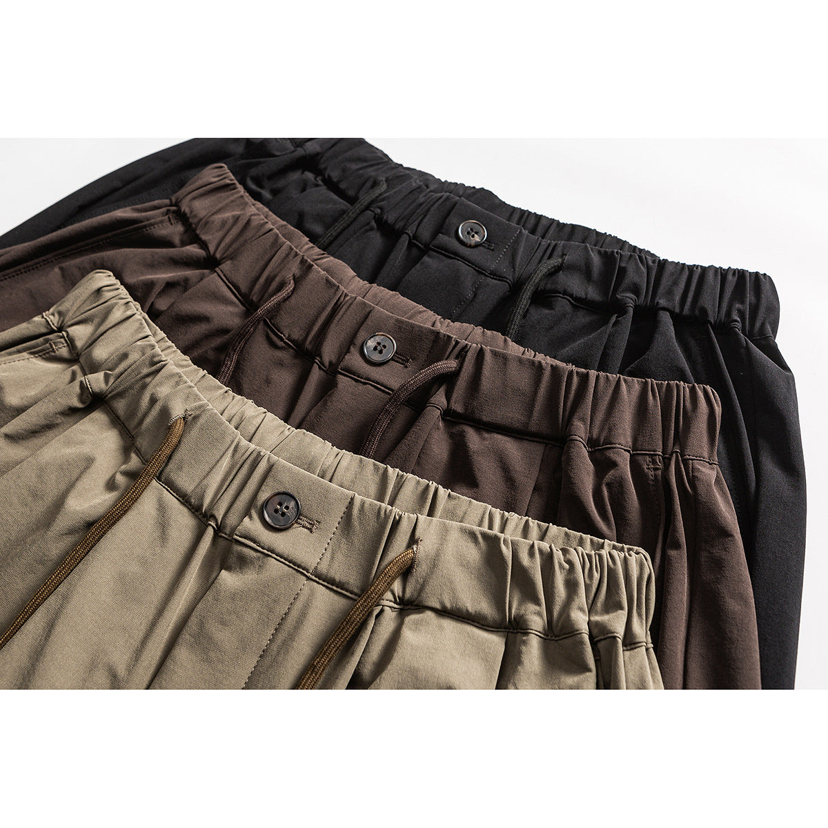 Close-up of three pairs of wide-leg pants in olive, dark brown, and black, showing elastic waistbands, buttons, and