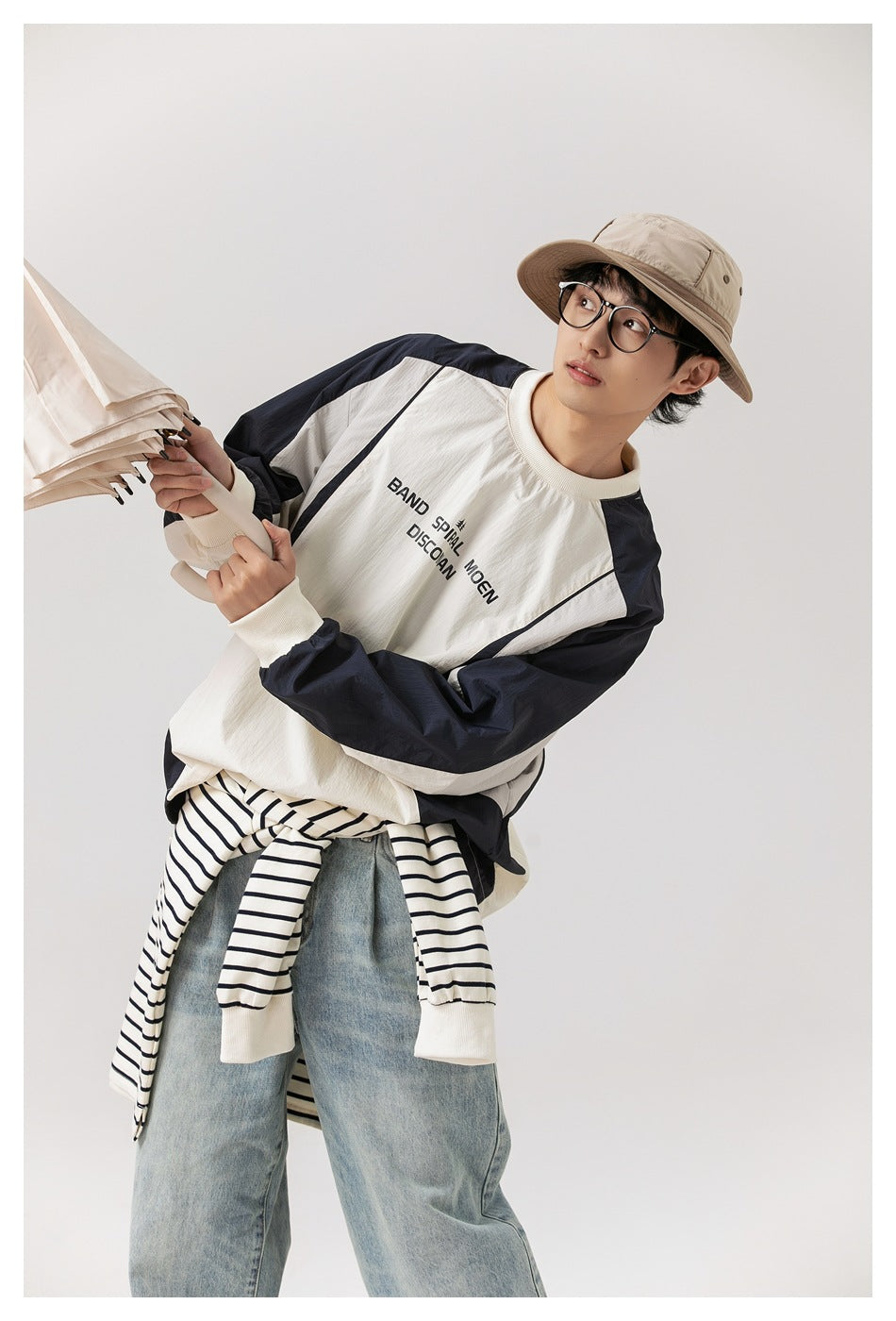 Model wearing an ivory and navy color-block pullover with a chest print, striped shirt tied at the waist, and light jeans.