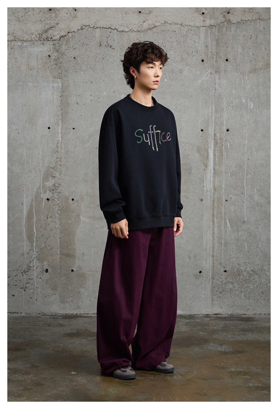 Three-quarter view of a model wearing a black sweatshirt with colorful chest lettering and loose burgundy pants.