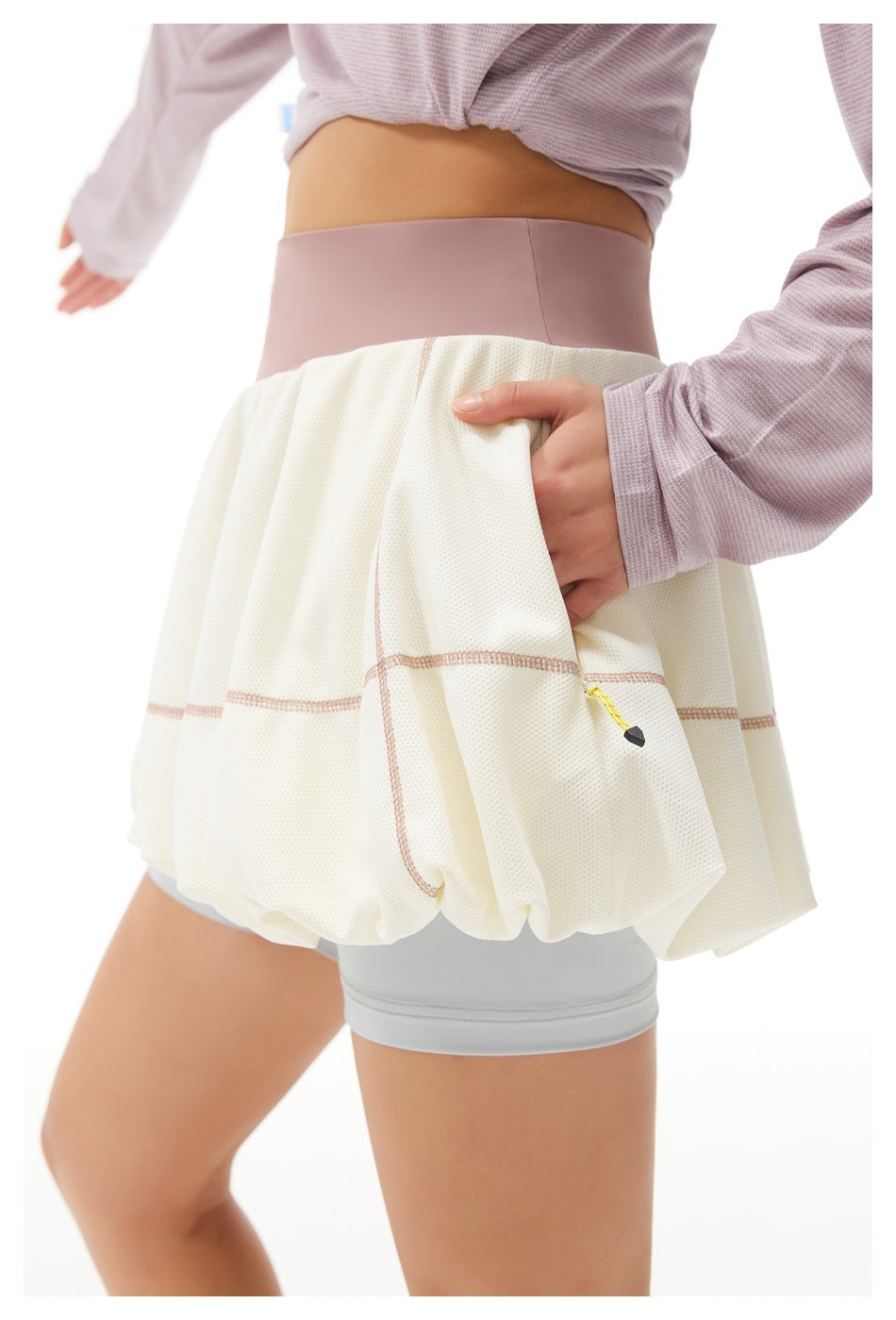 Close-up of an ivory bubble tennis skirt with mauve waistband, pink contrast stitching and a small yellow zipper.