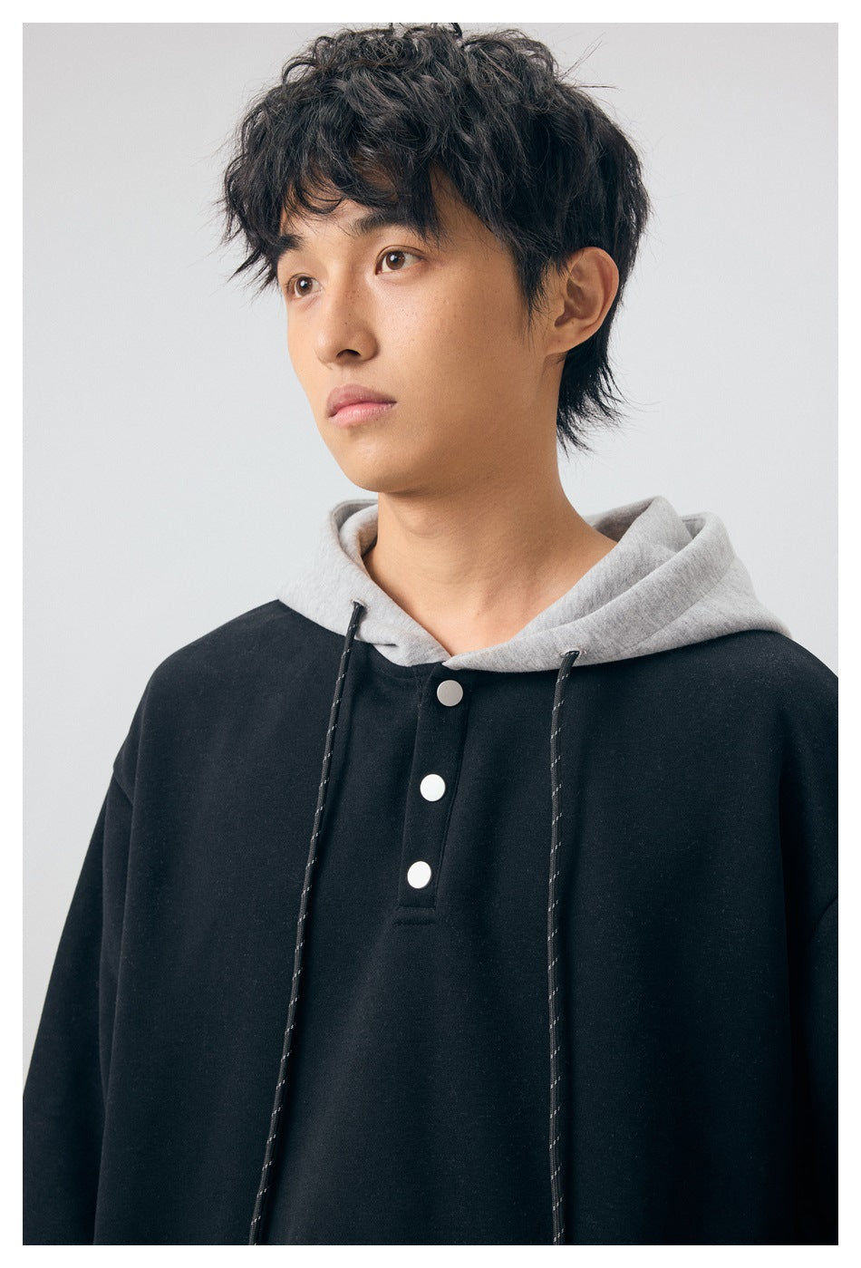Close view of a model wearing a black hoodie with a contrasting gray hood, drawstrings, and three-button placket.
