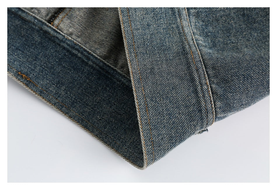 Close-up of overlapping blue denim panels with orange stitching and a folded, pointed seam.