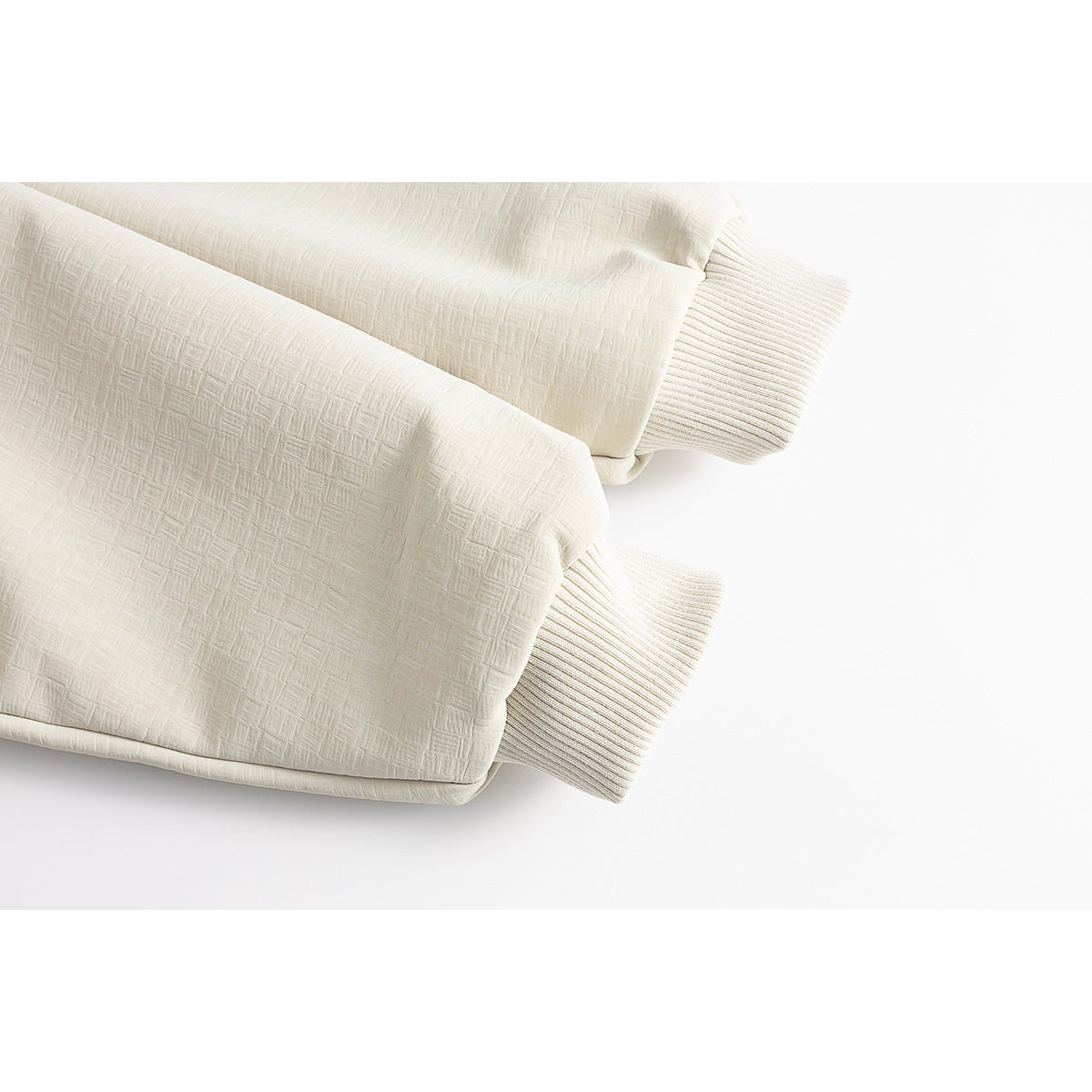 Close-up of two ivory jacket sleeves with ribbed cuffs and textured outer fabric.