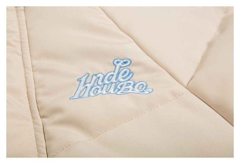 Close-up of blue-and-white embroidered lettering on the beige jacket fabric.