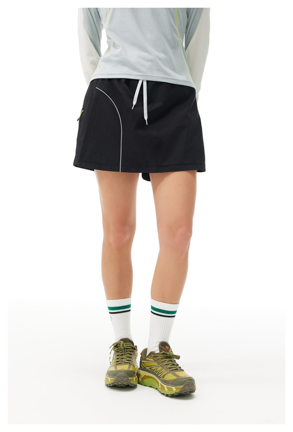 Rear view of a model wearing a black athletic skort with white drawstrings and curved gray piping.