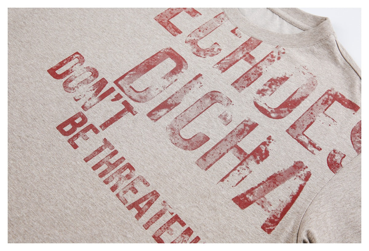 Angled close-up of a beige T-shirt's distressed red front print and crew neckline.
