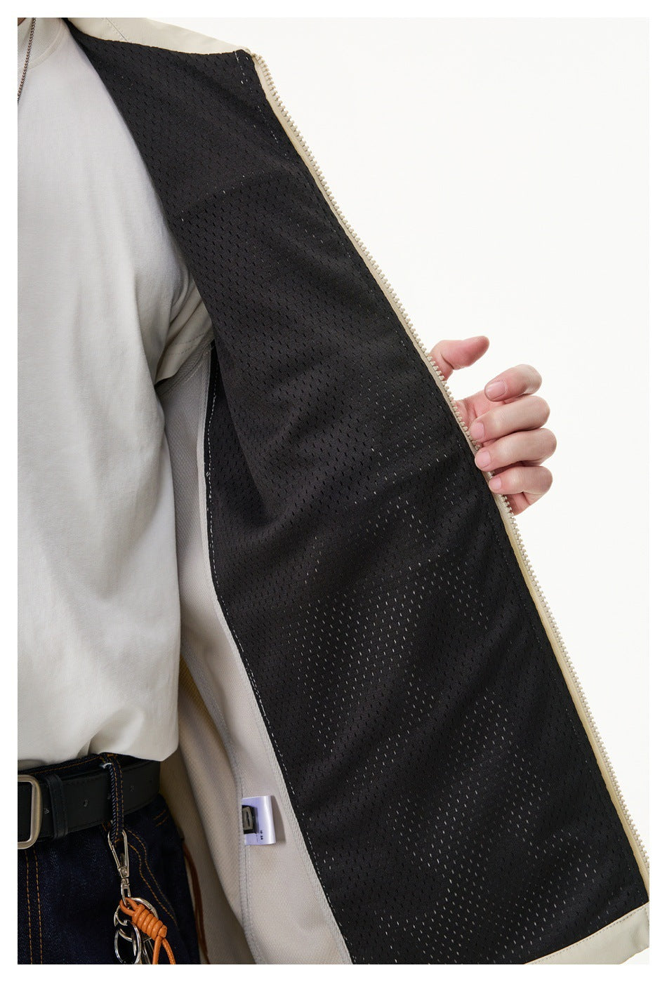 Close-up of an open light beige jacket showing its black mesh lining and pale zipper.