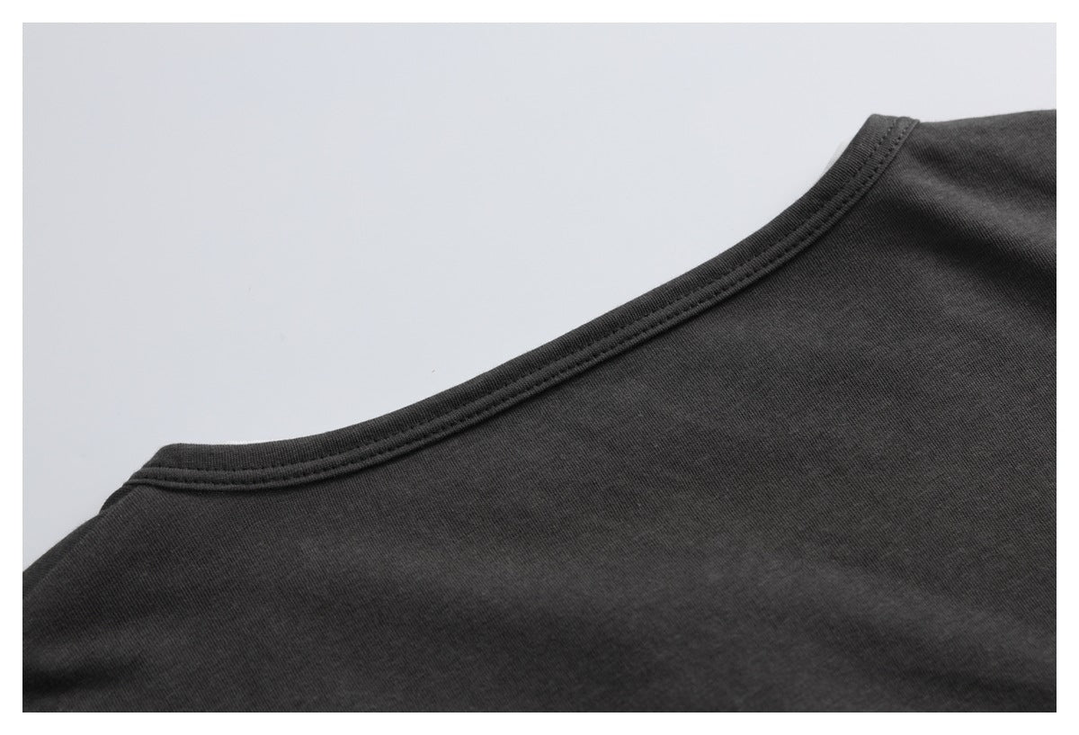 Close-up of a charcoal-black shirt’s rounded neckline and stitched edge against a light background.