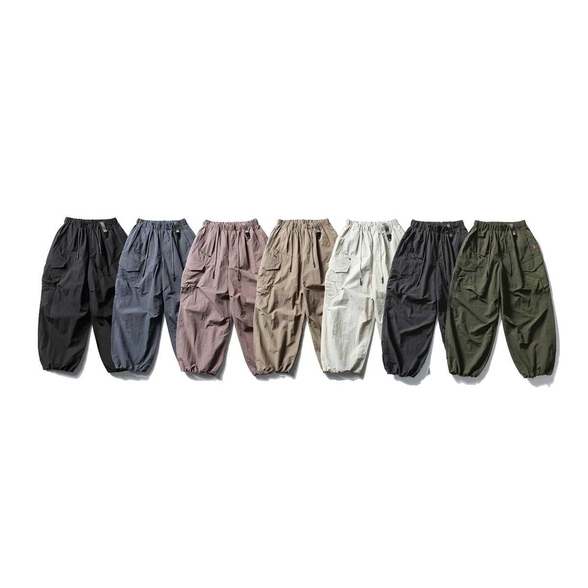 Seven pairs of loose cargo trousers shown together in black, blue-gray, mauve, taupe, off-white, charcoal and olive.