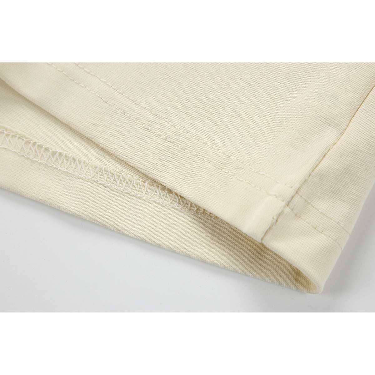 Close-up of a cream garment hem showing the folded edge, double stitching, and interior overlock seam.