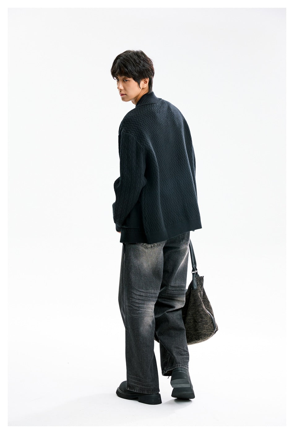 Rear three-quarter view of a model wearing a dark patterned knit cardigan with a ribbed stand collar.
