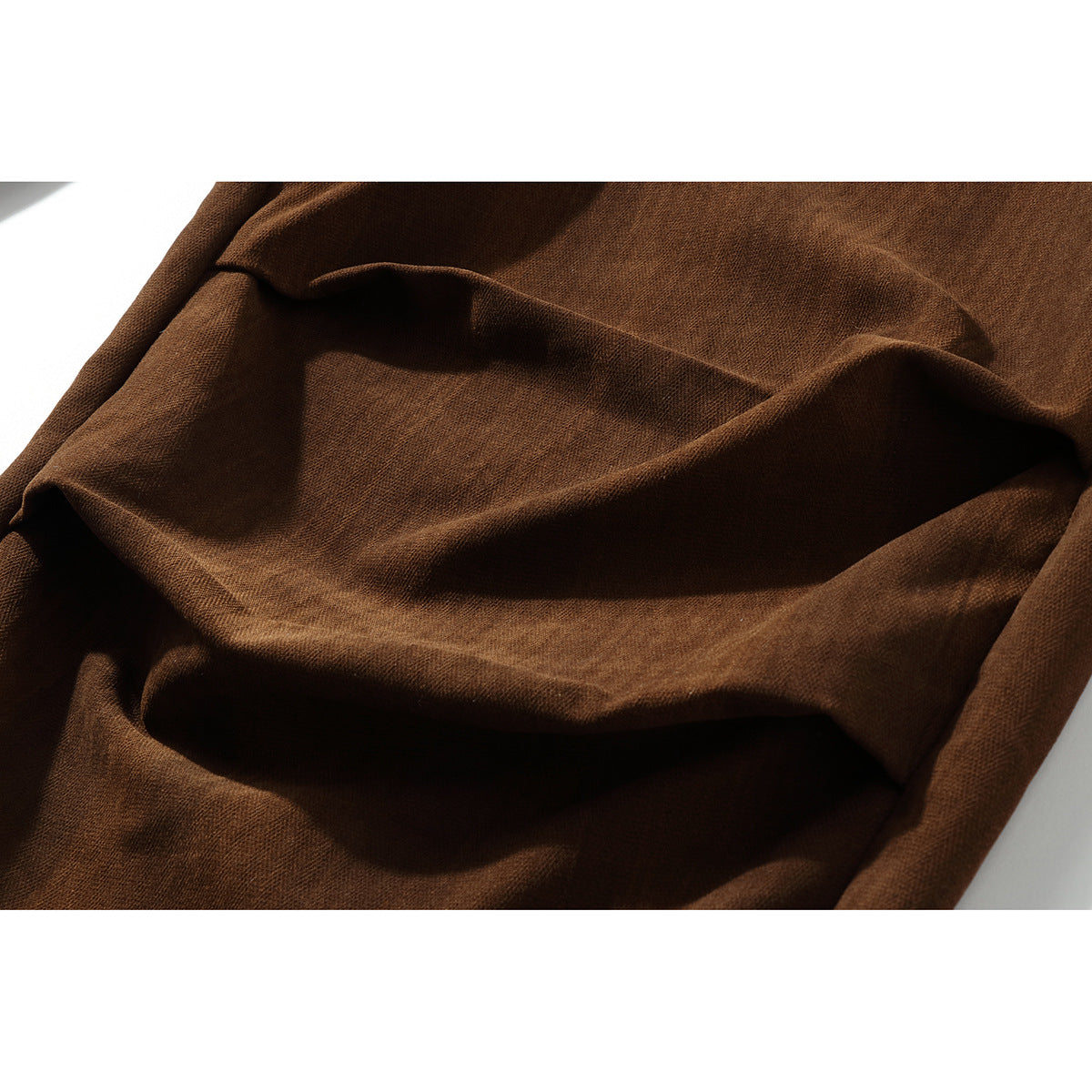 Macro view of the brown trousers' textured fabric and soft folds.
