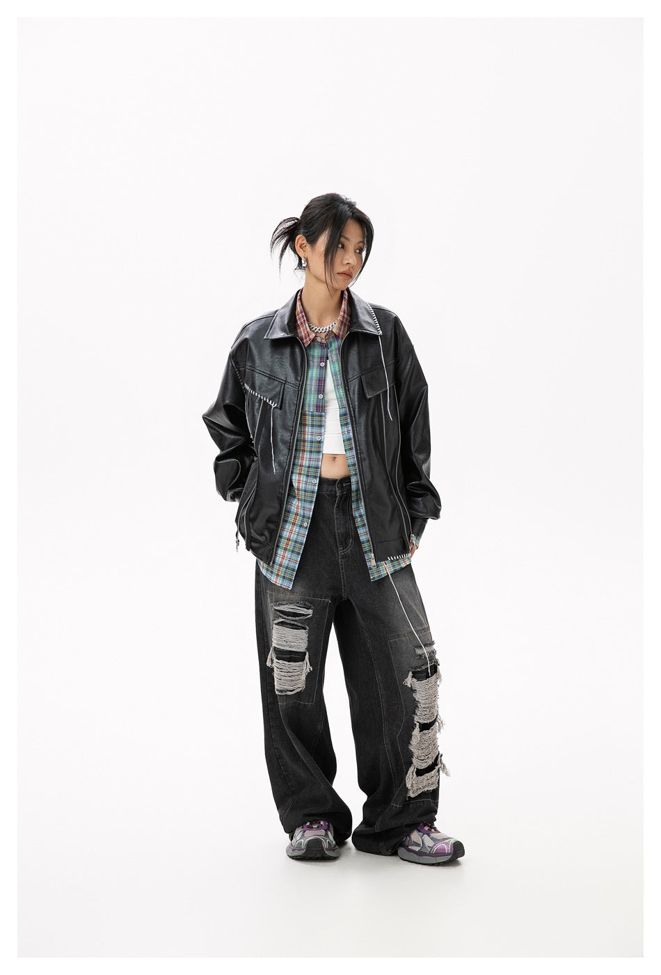 Model wearing a black jacket with white stitch details over a colorful plaid shirt.