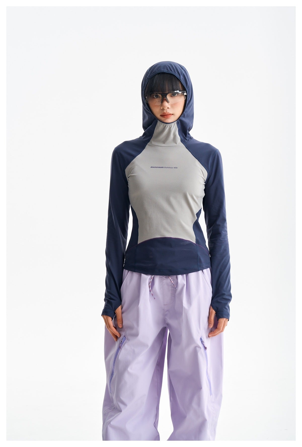 Front view of a model wearing a navy and gray hooded top with loose lavender pants.