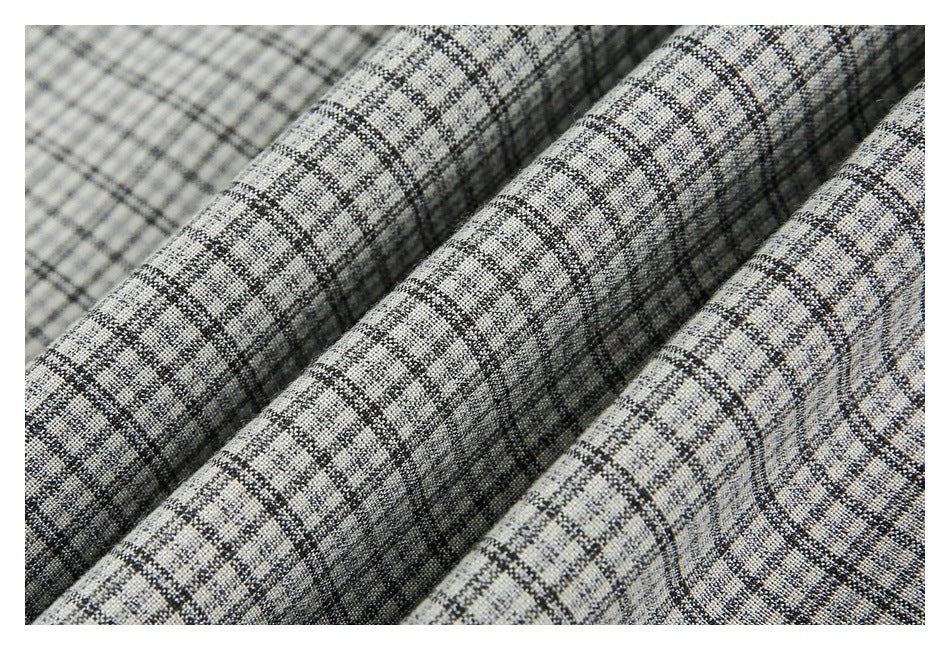 Close-up of gray and black plaid fabric gathered into several folds, showing its textured weave.