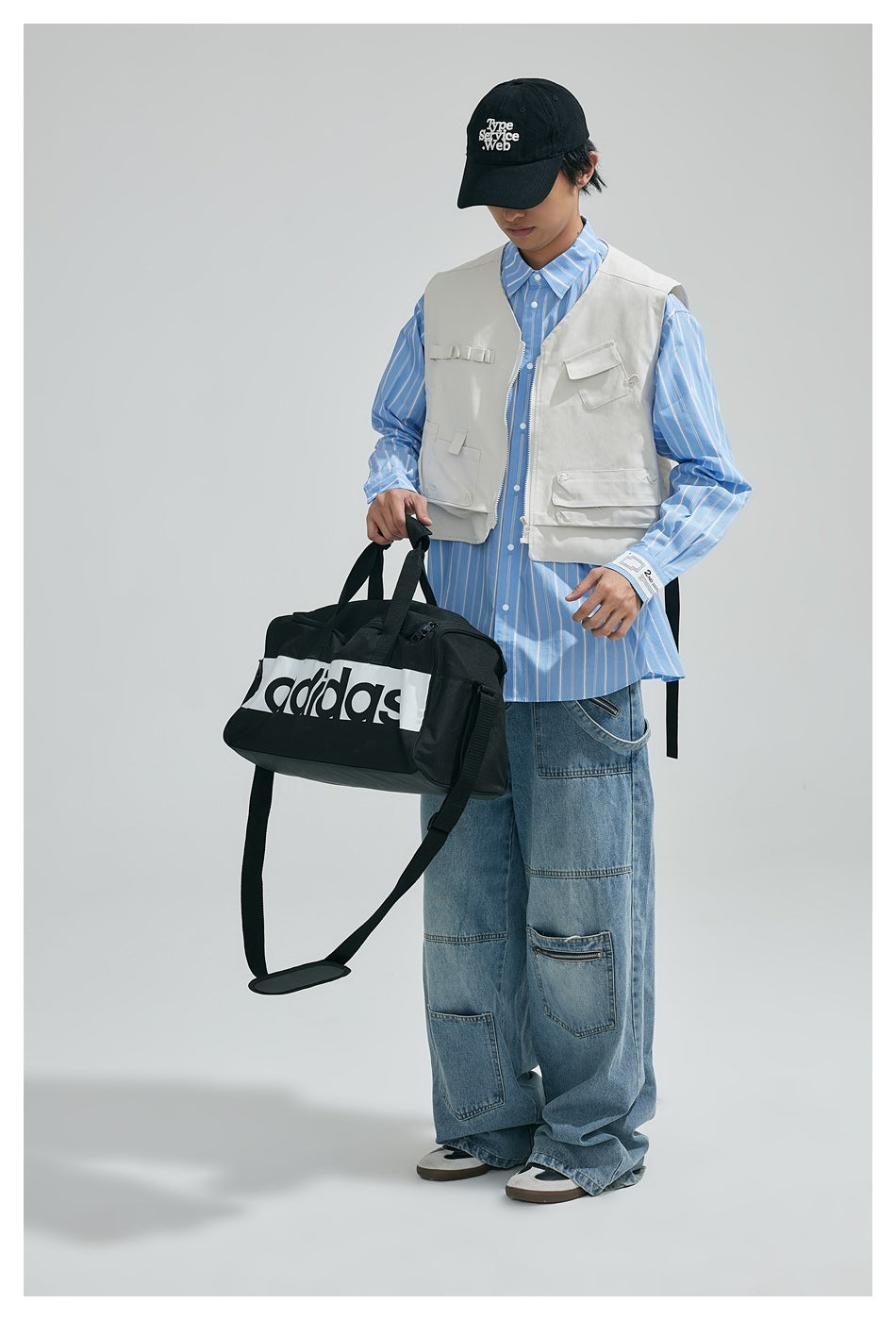Model wearing a white pocketed utility vest over a blue striped shirt with loose jeans.