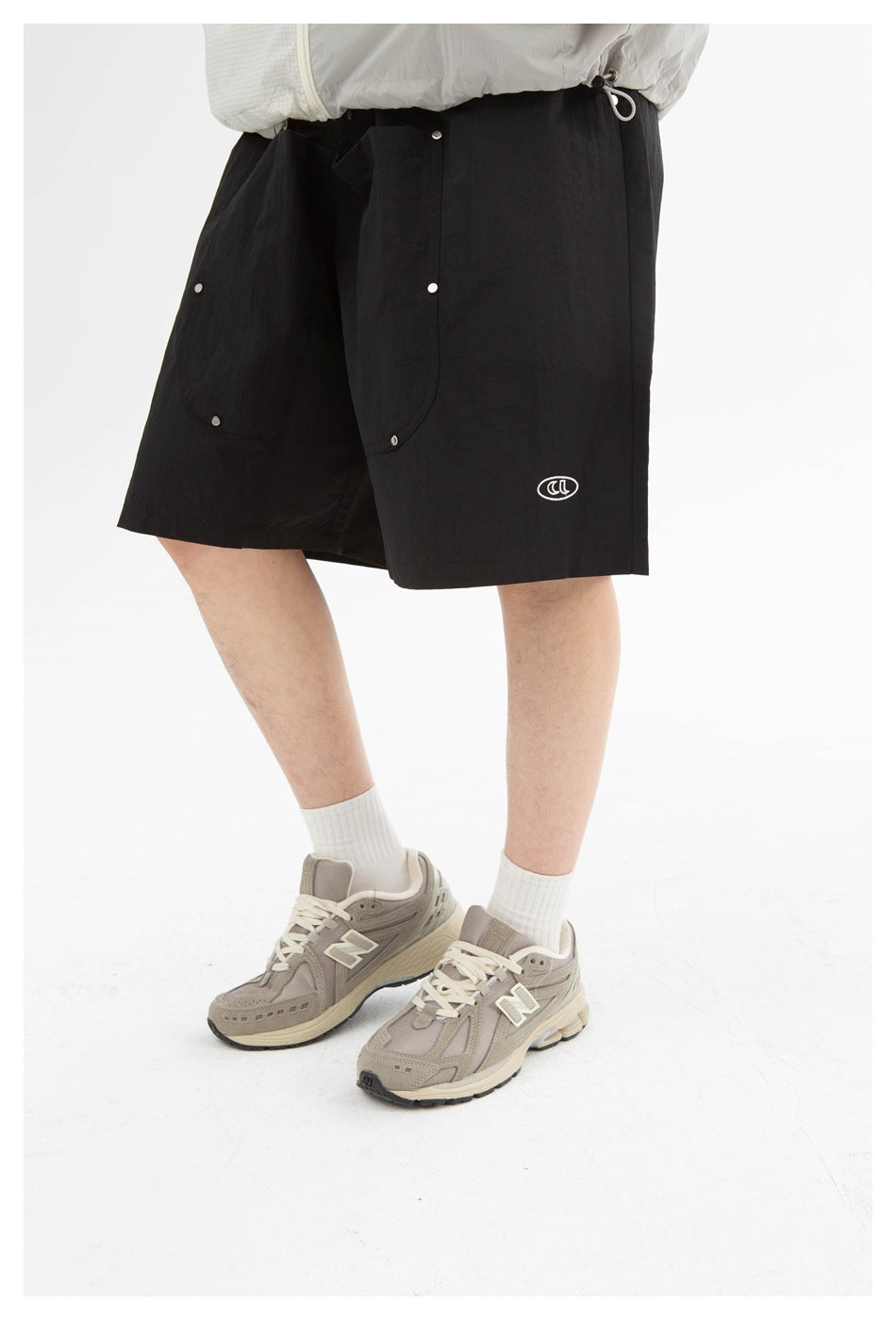 Person wearing black knee-length shorts with snap-fastened front panels and a small white oval emblem.