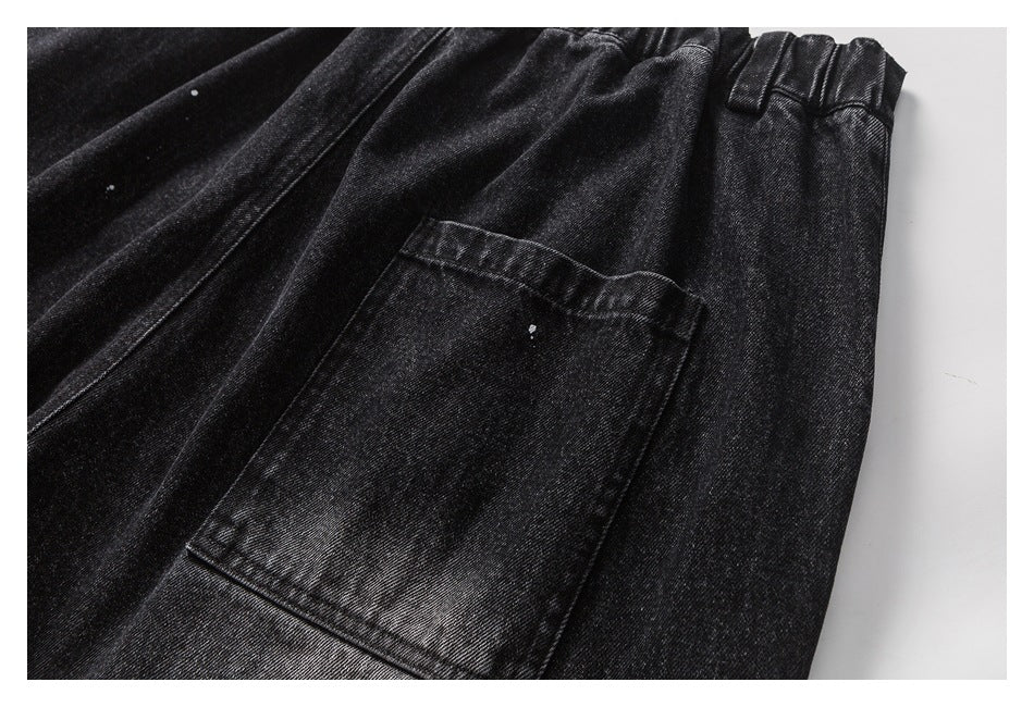 Close-up of black denim trousers showing a large patch pocket, elastic waistband and white specks.