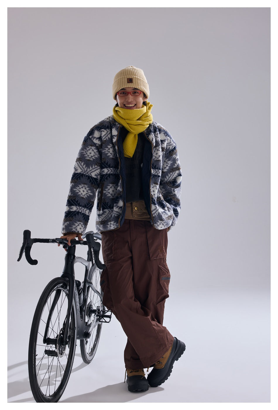 Front view of a model wearing a blue-gray and white geometric fleece jacket beside a bicycle.