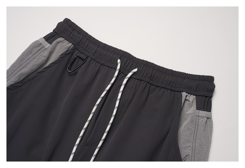 Close-up of charcoal pants showing the elastic waistband, white drawstrings, metal clip, and gray side pocket panels.