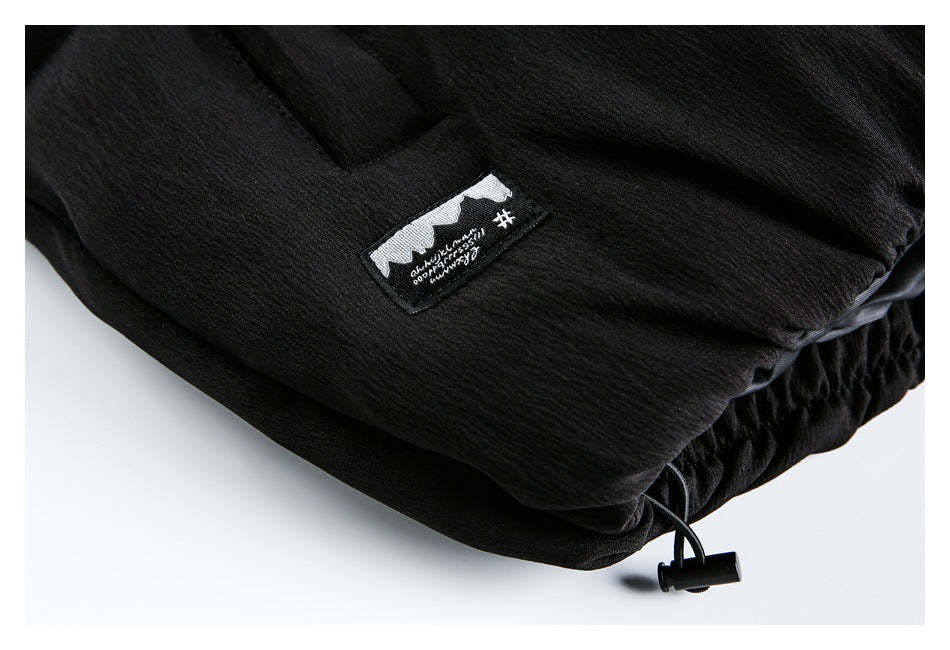 Close-up of a black garment's hem, drawcord toggle, and small sewn black-and-white label.