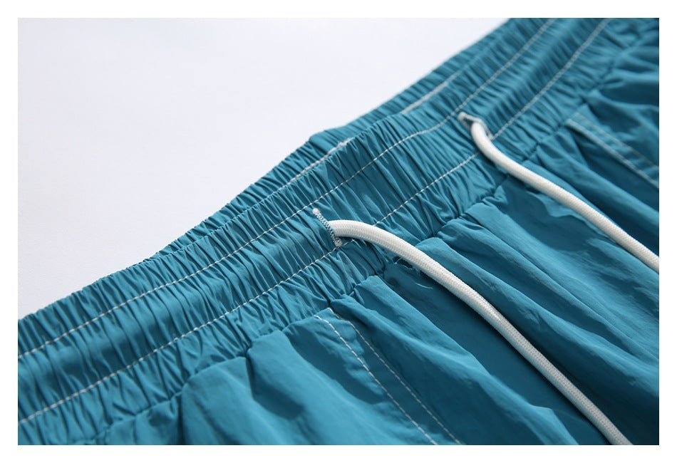 Close-up of the turquoise shorts' elastic waistband, white drawstrings, and stitched seams.