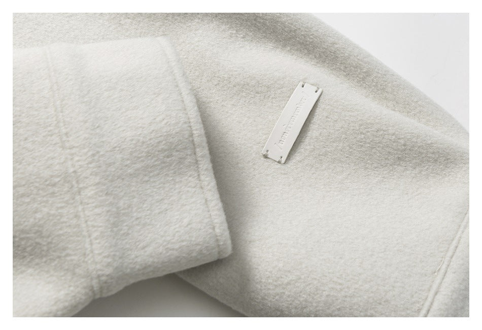Close-up of an off-white coat seam and a small rectangular metal nameplate.