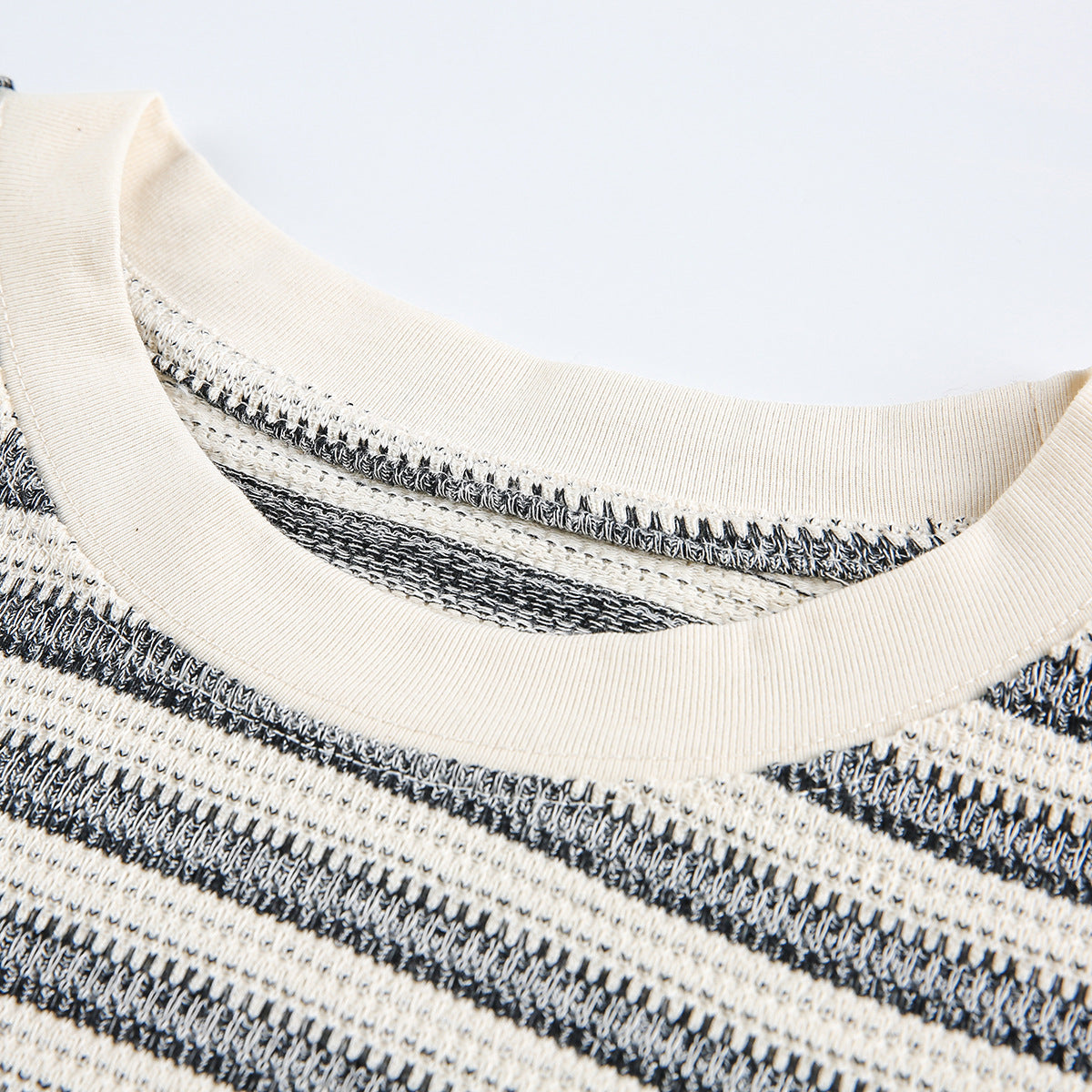 Close-up of a cream ribbed crew neckline and black-and-cream horizontal stripes on a knit shirt.