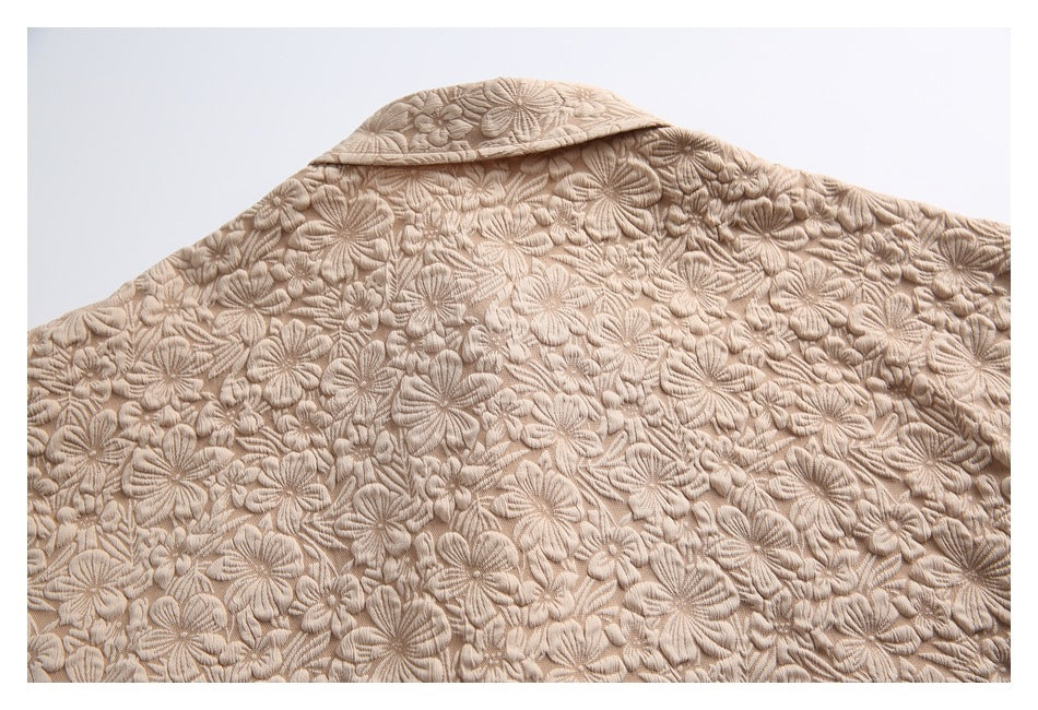 Back of a beige shirt with a collar and dense raised floral texture, laid flat.