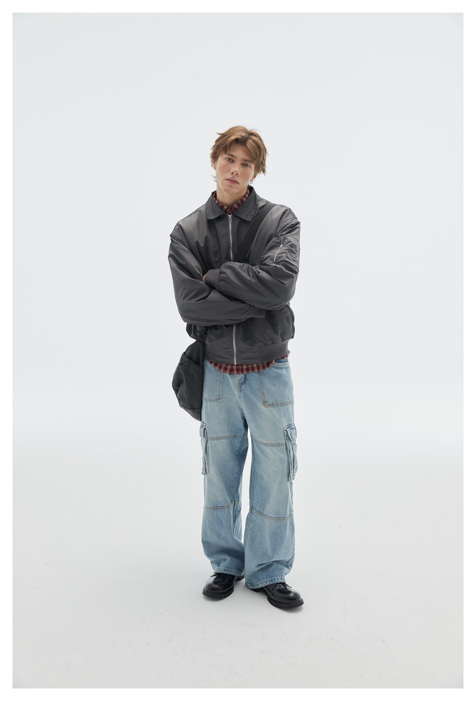 Model wearing a charcoal zip-front jacket with a sleeve pocket, light blue cargo jeans, and a black crossbody bag.