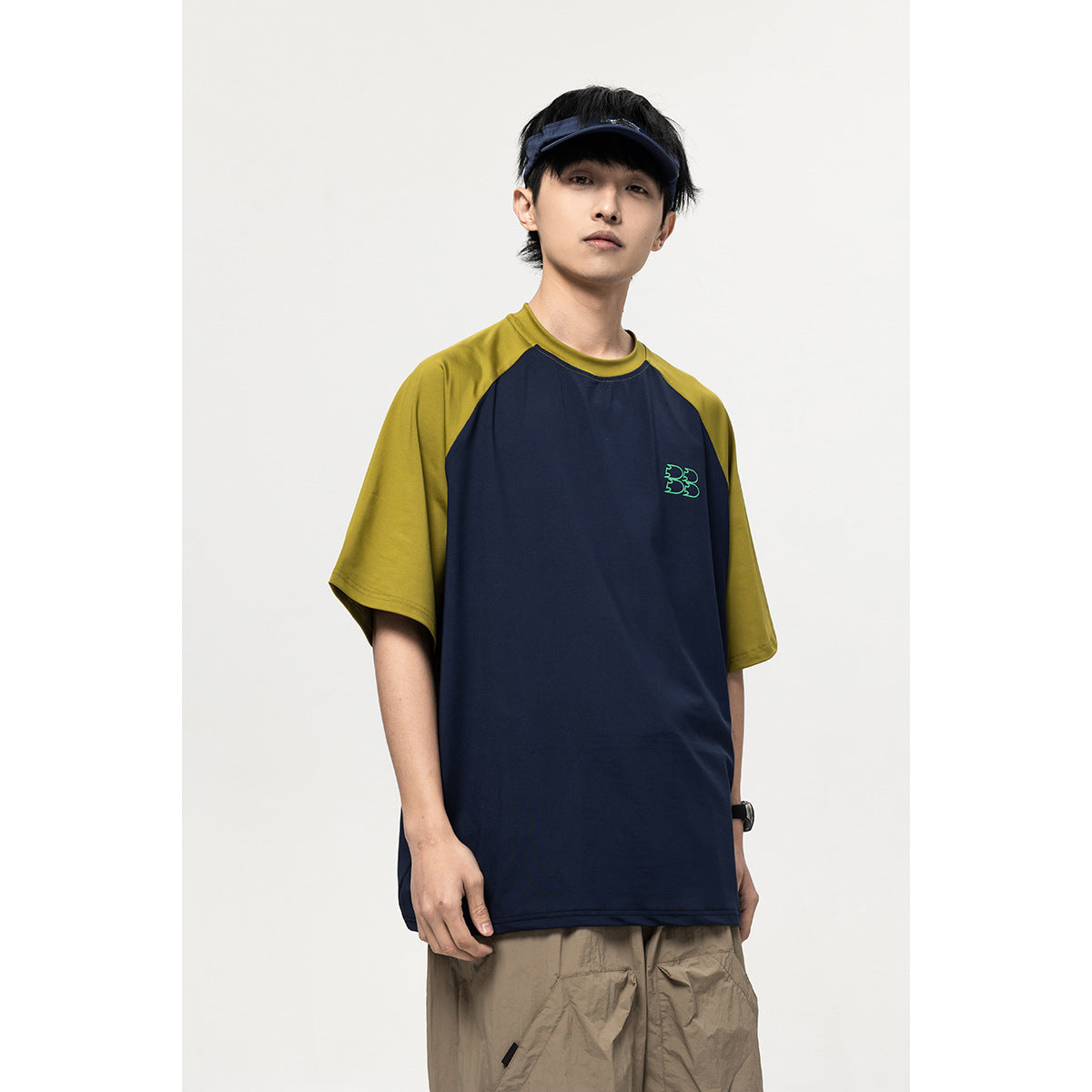 Model wearing a navy T-shirt with olive raglan sleeves and a small green chest graphic, shown from the front.