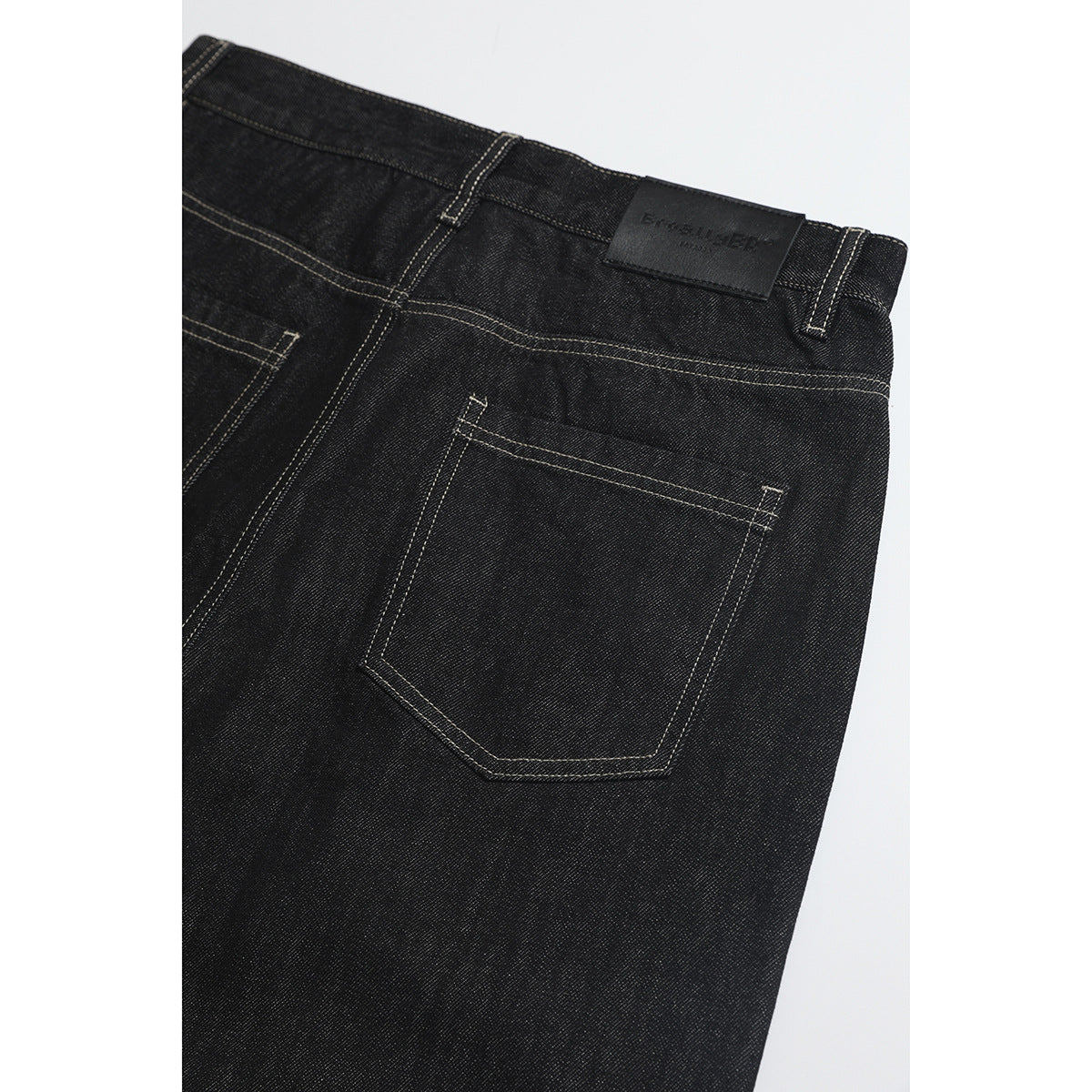 Close-up of the back of black jeans, showing a patch, waistband, stitching and a single rear pocket.