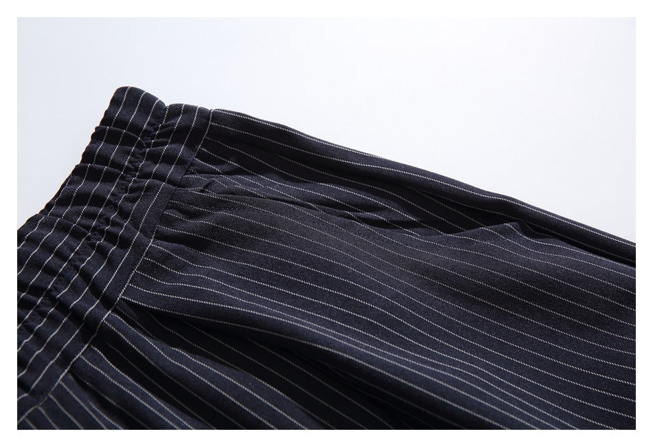 Close-up of dark pinstriped trouser fabric and gathered waistband, laid flat.
