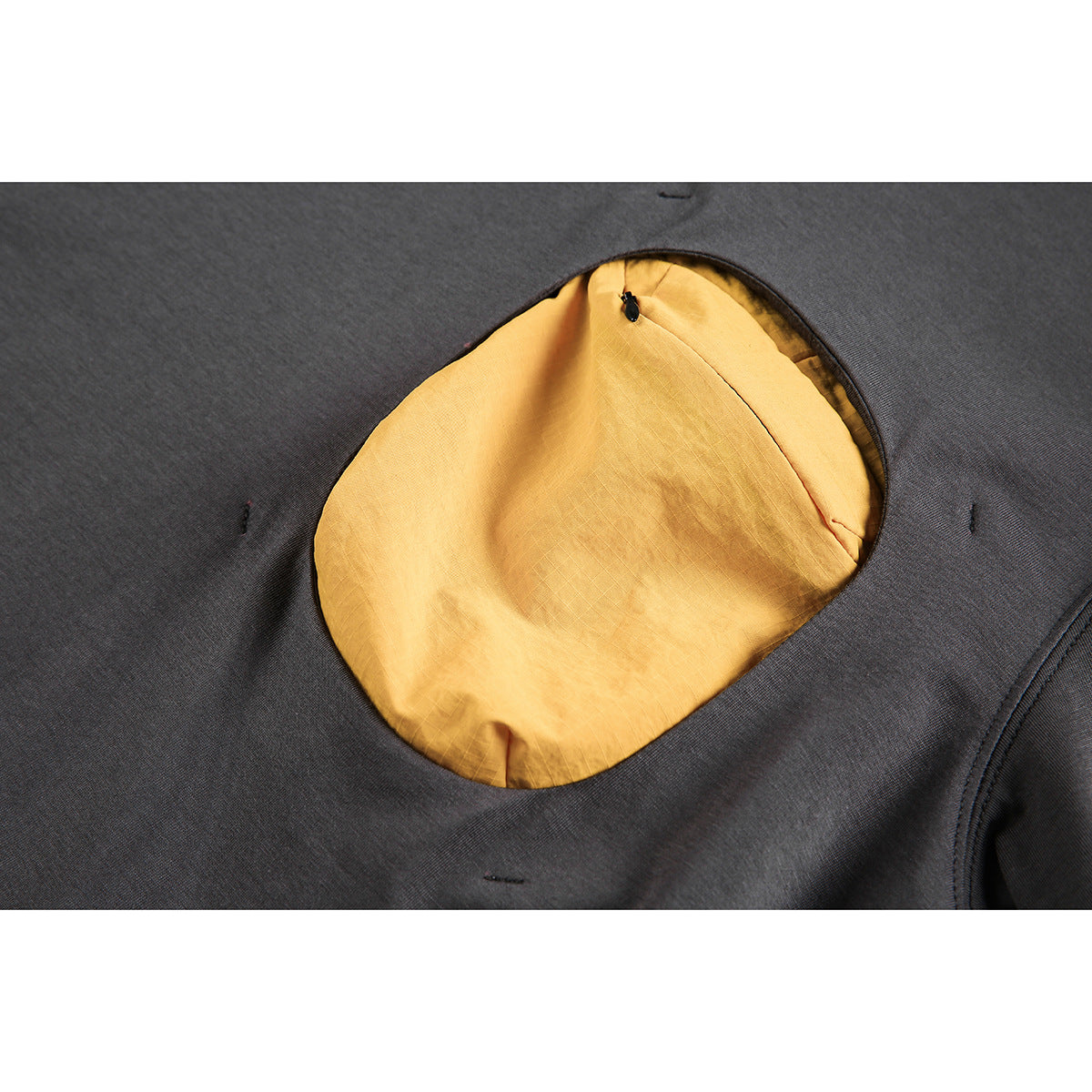 Close-up of a charcoal garment with a rounded opening revealing mustard-yellow lining and a small zipper.