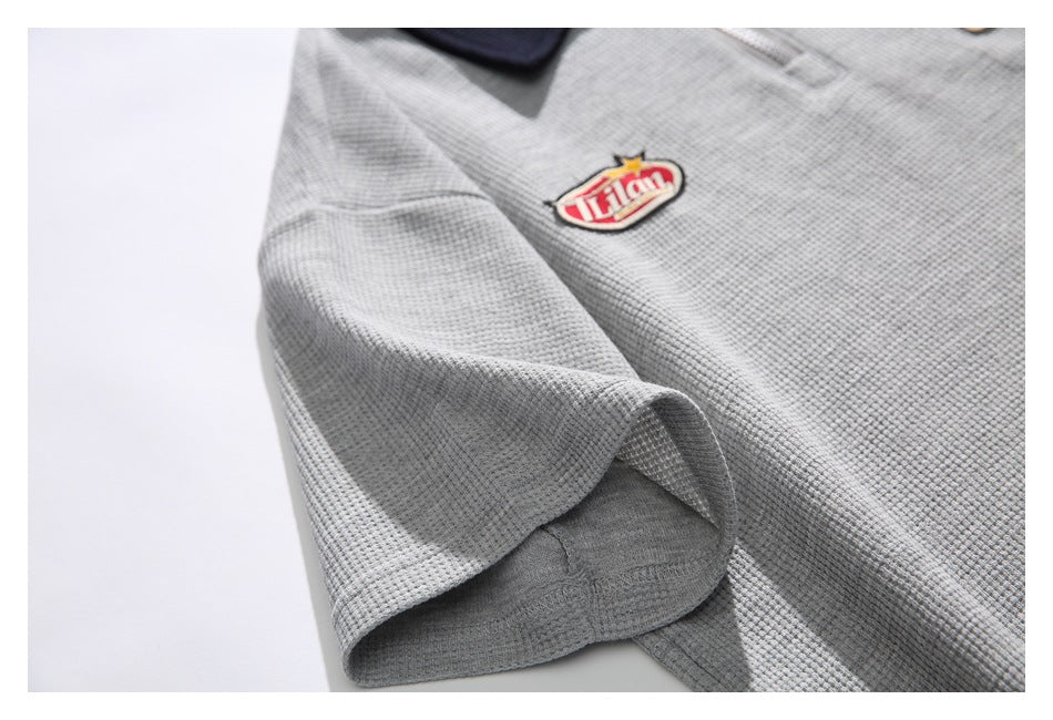 Close-up of the pullover's short sleeve and hem seam, with an embroidered chest patch visible.