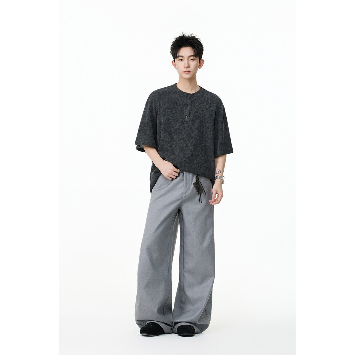Full-length model wearing an oversized charcoal henley shirt, wide gray trousers, and black shoes.