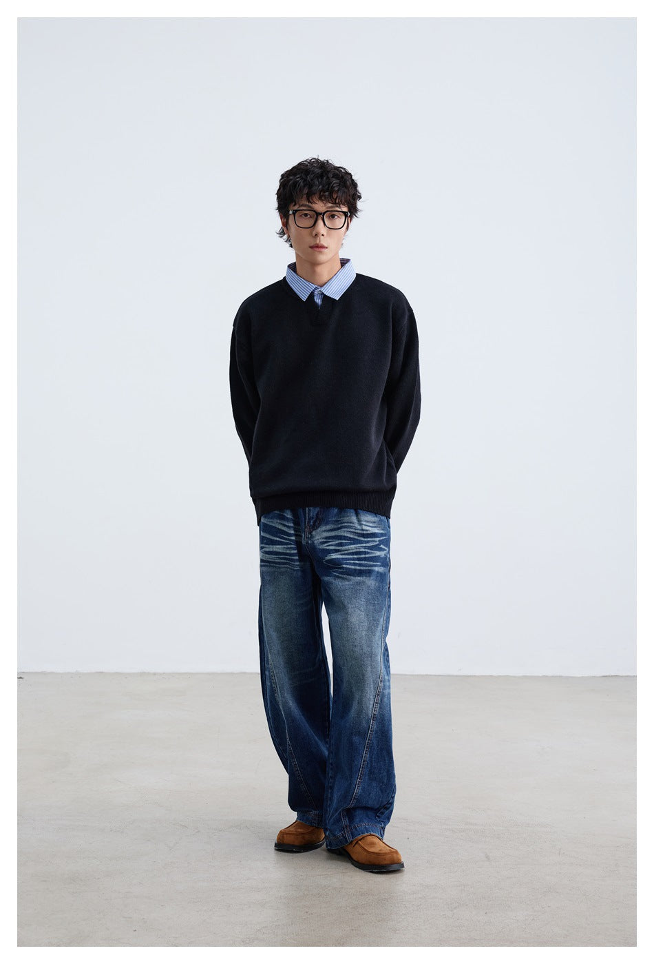 Full-length model wearing a black V-neck sweater over a blue striped shirt with loose blue jeans.