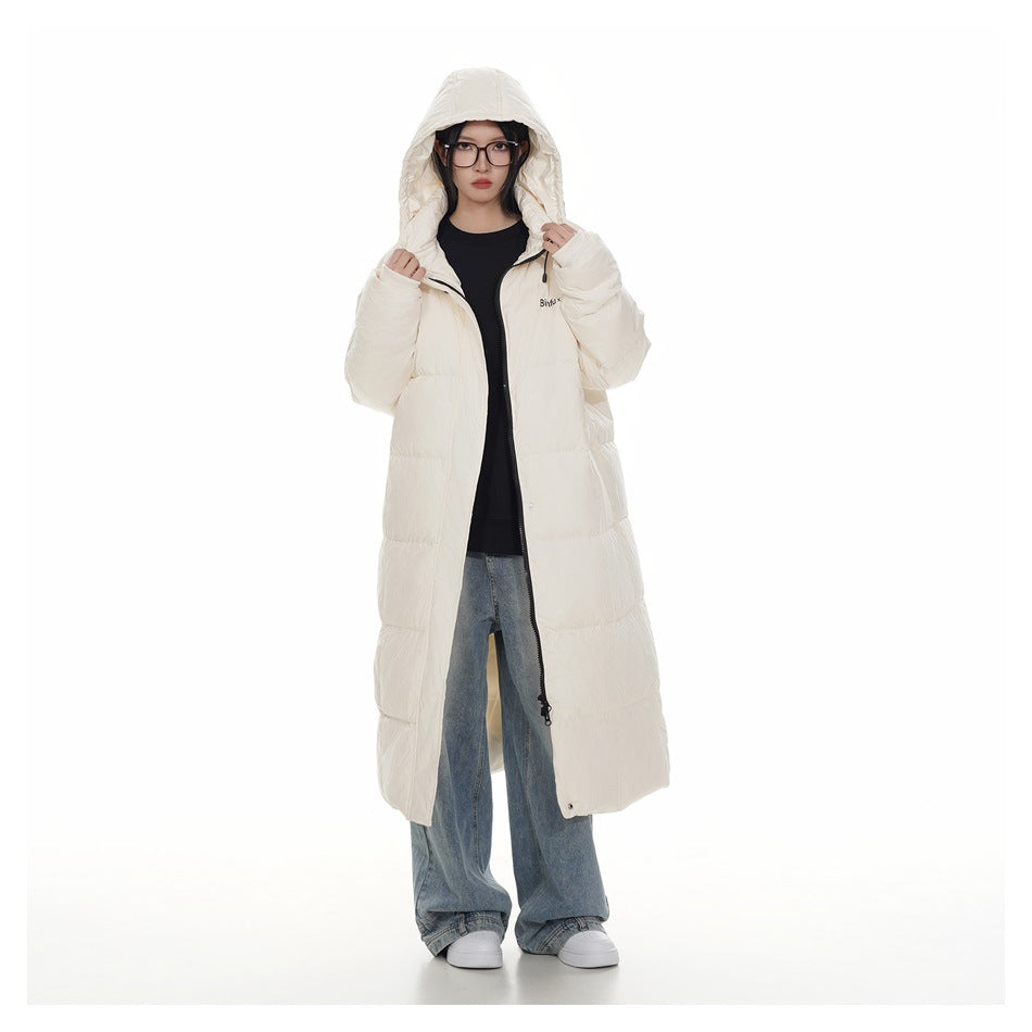 Model wearing a long ivory puffer coat with the hood up, open over a black top and blue jeans.