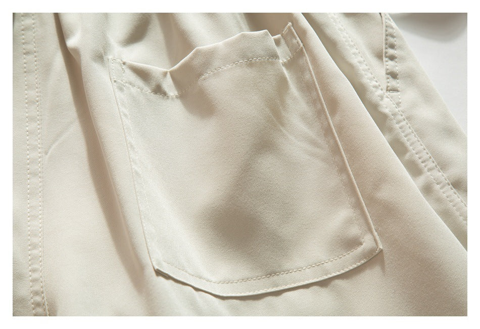 Close-up of light beige trousers showing a large rectangular patch pocket and stitched seams.